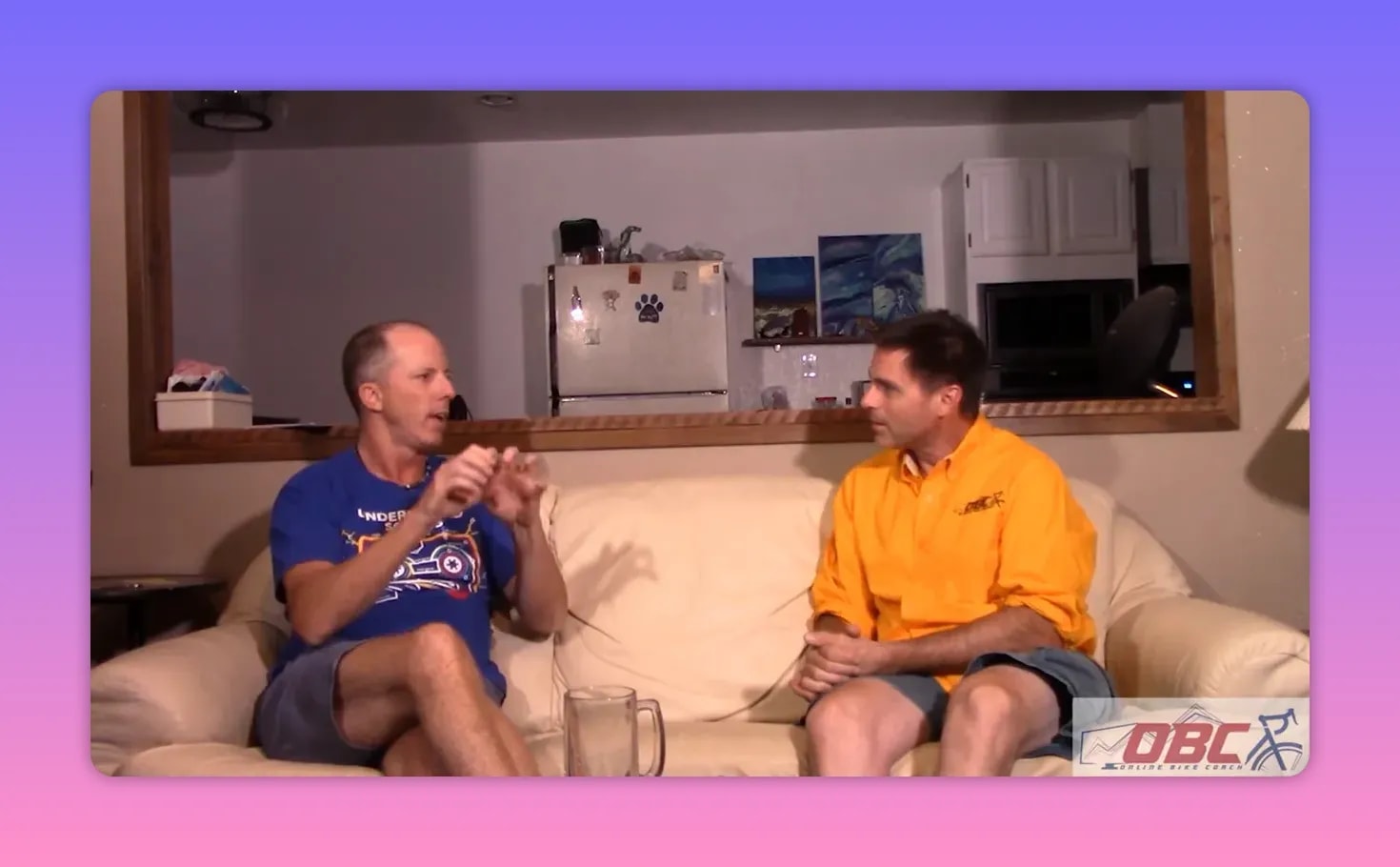 Two people talking on a couch; left speaker forming small precise hand gestures while explaining