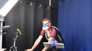Cyclist on an indoor trainer wearing a VO2master metabolic mask during a Billat 90/90 interval session with a Garmin 1040 and camera setup for data documentation.