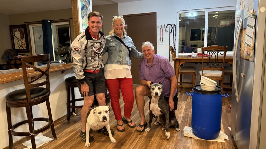 Murray and Cynthia in the kitchen smiling while posing with two dogs during a dinner visit.