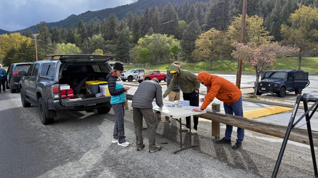 A group of people in cold-weather gear and puffer jackets registering for a bike race at an outdoor folding table in misty, windy Reno, Nevada.