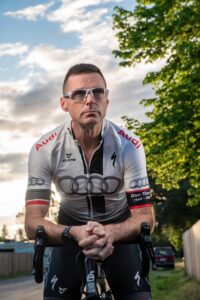 Professional profile shot of Richard Wharton, a veteran cycling coach, smiling and looking confidently slightly off-camera.