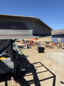 A compact utility tractor equipped with a front loader bucket parked on a dirt site during the initial prep and construction phases of a container home build.