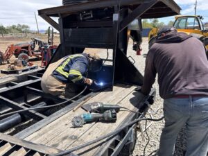 Industrial steel frame structure of a custom trailer under construction on a concrete shop floor, showcasing heavy steel pipe and structural fabrication.