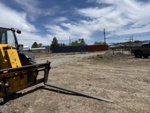 A large, heavy-duty commercial forklift and telehandler parked on an outdoor gravel and dirt lot, used for moving heavy steel and building components.