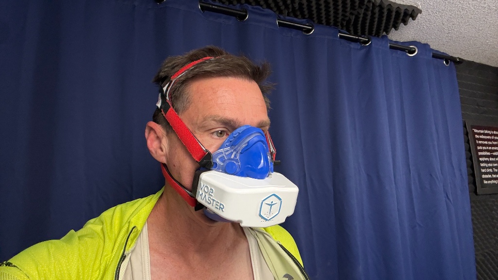 Coach Wharton conducting indoor cycling metabolic testing using a gas analyzer mask and muscle oxygen sensors.
