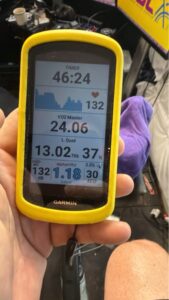 A hand holding a Garmin Edge cycling computer with a yellow protective case, displaying real-time physiological metrics including a workout timer at 46:24, heart rate at 132 bpm, VO2 Master at 24.06, left quad muscle oxygenation at 37%, and an alphaHRV score of 1.18.