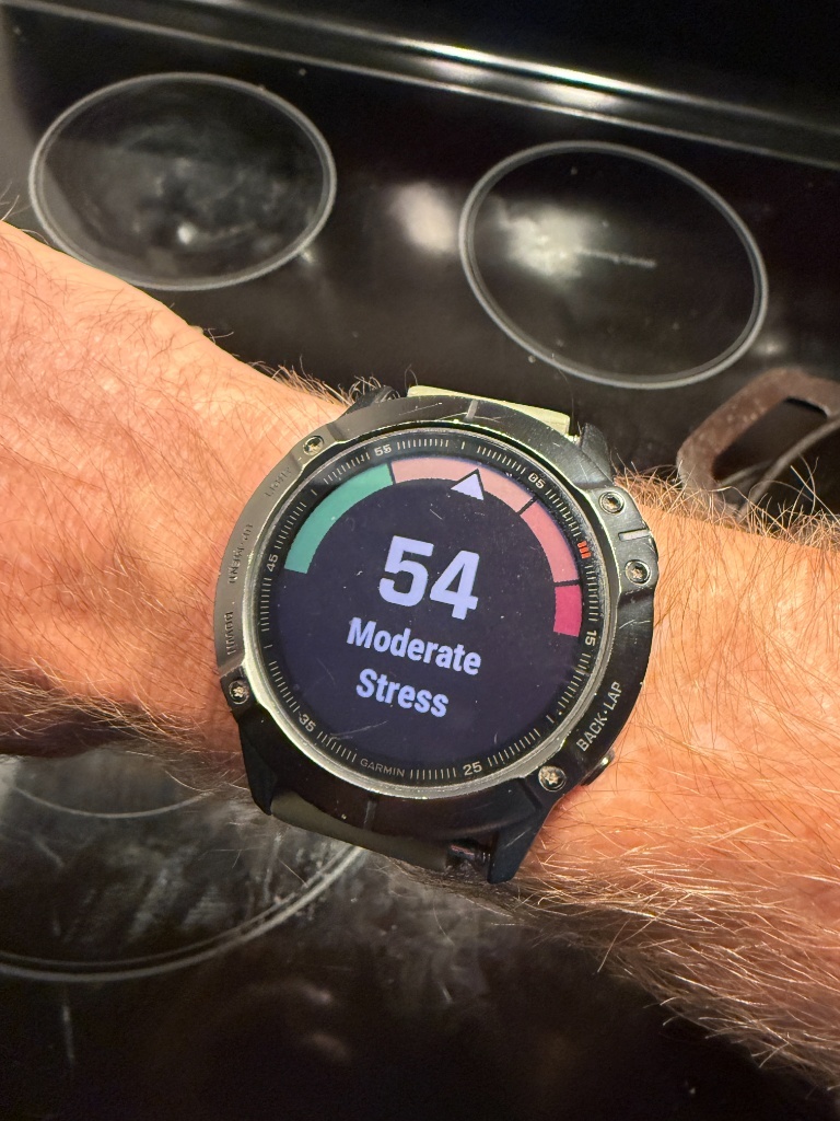 Garmin smartwatch on a wrist displaying a real-time HRV Stress score of 54 indicating moderate stress.